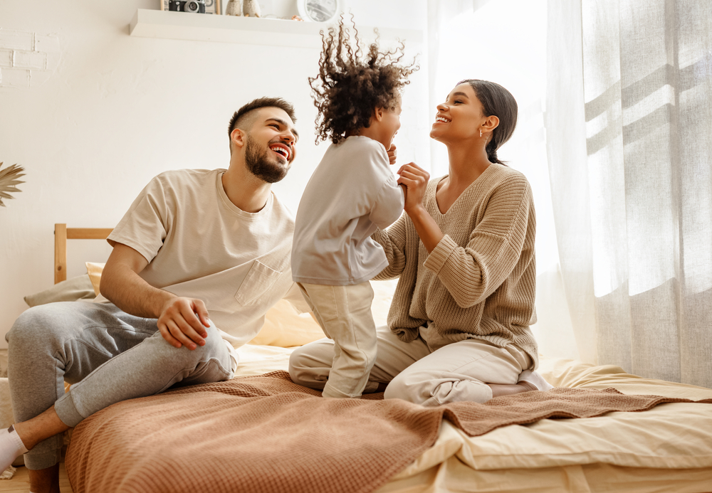 Happy family spending time together on bed, with parents laughing and child playing joyfully, symbolizing love, bonding, and cherished moments
